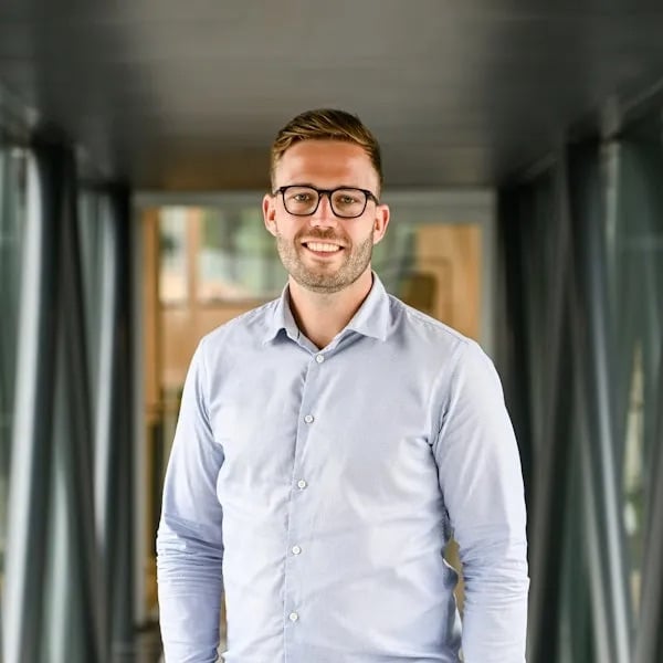 Man kijkt lachend de camera in en staat in de gang.