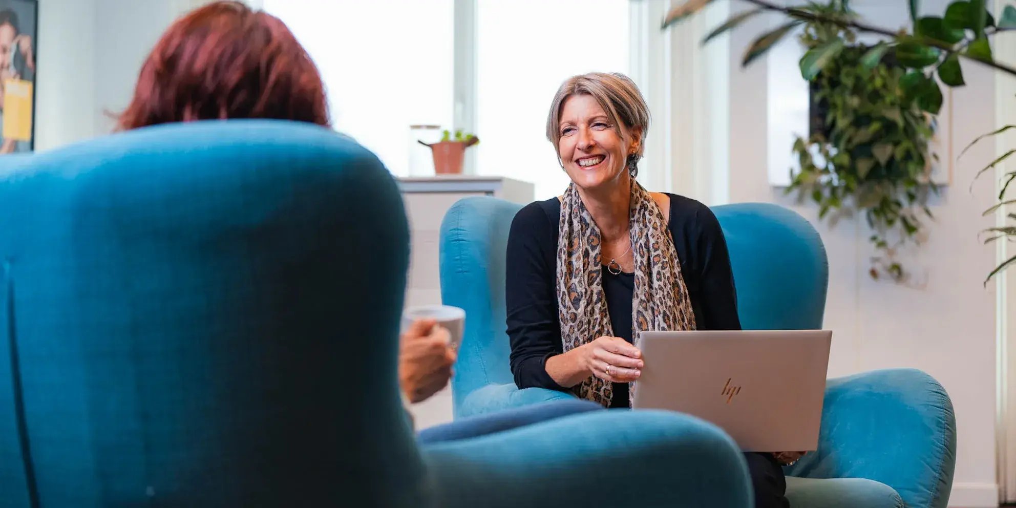 Vrouw met laptop lacht tijdens informeel gesprek op kantoor.