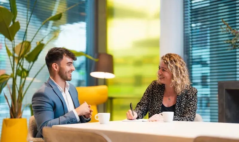 Man and woman at a table with coffee, laughing at each other.