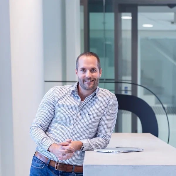 Man leunt op een hoge tafel en kijkt lachend voor zich uit.