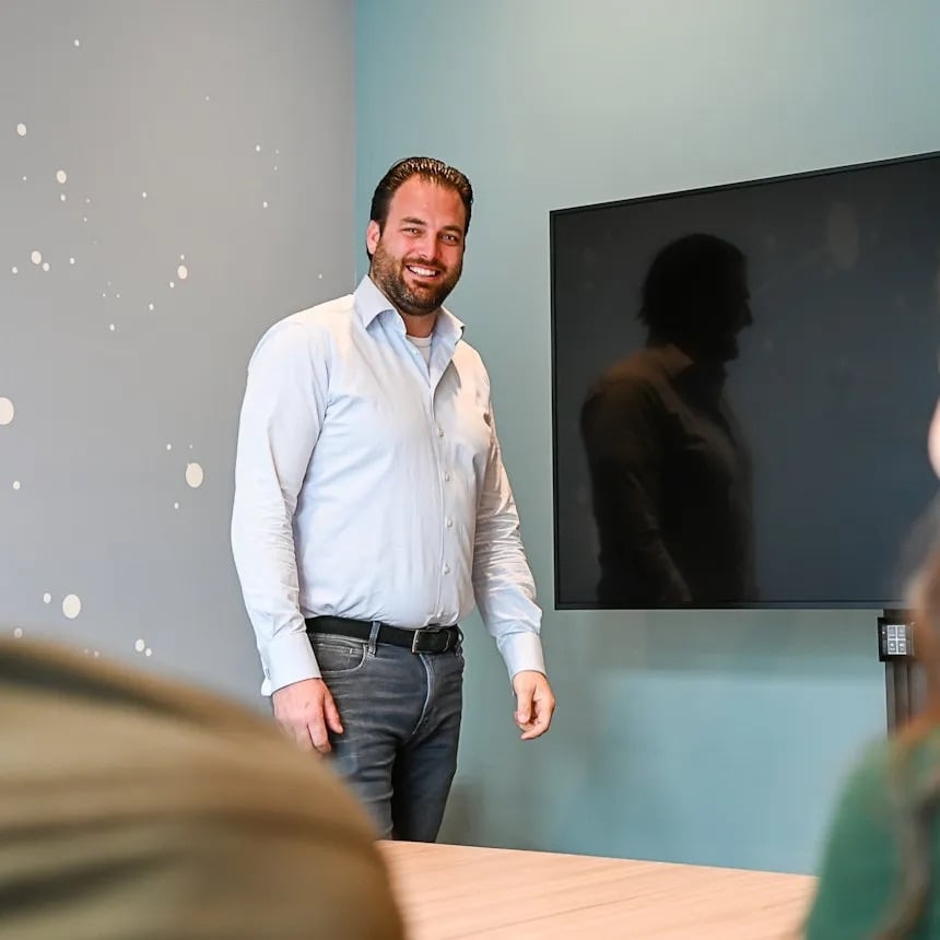 Man staat in een meetingruimte en kijkt lachend op.