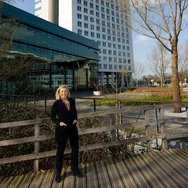 Vrouw op een houten brug met een modern gebouw op de achtergrond.