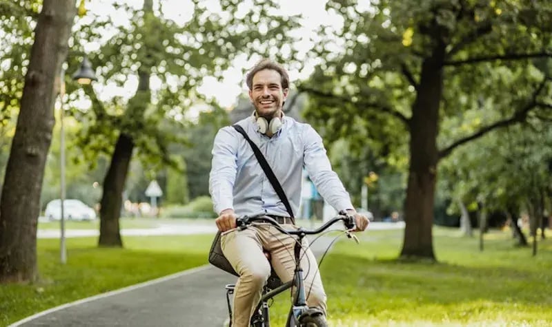 Man met donker haar in een park op de fiets lachend in de camera