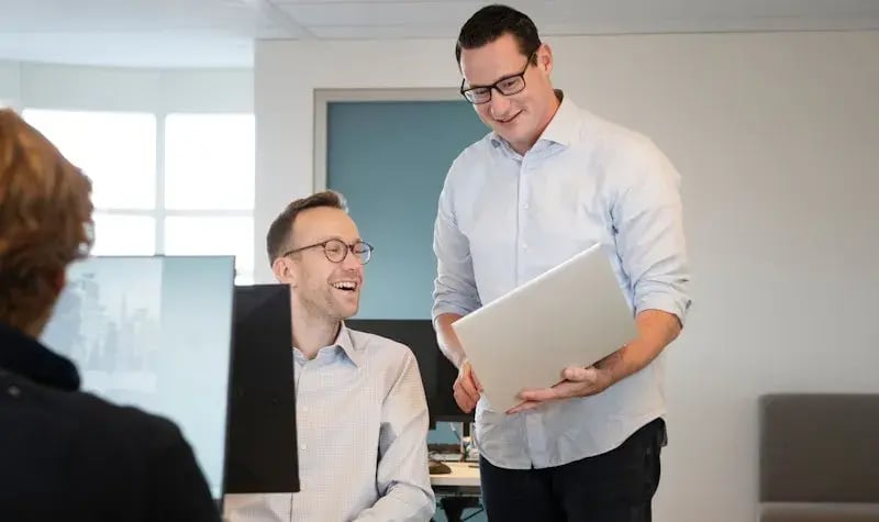 Twee mannen naast elkaar lachend met laptop voor hun