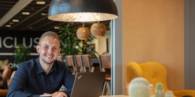 Man zit in de kantine met zijn laptop en lacht voor zich uit.