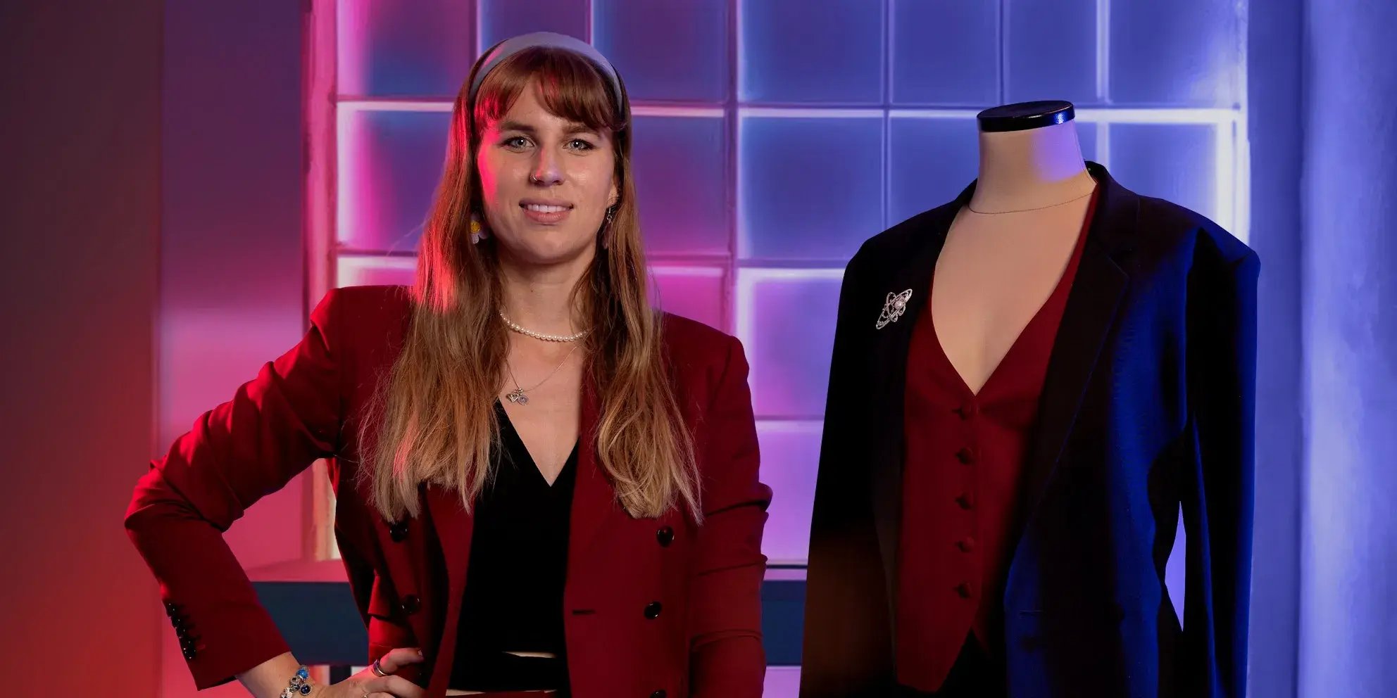 Glimlachende man met bril in een beige overhemd staat in een kantoor naast twee computerschermen.