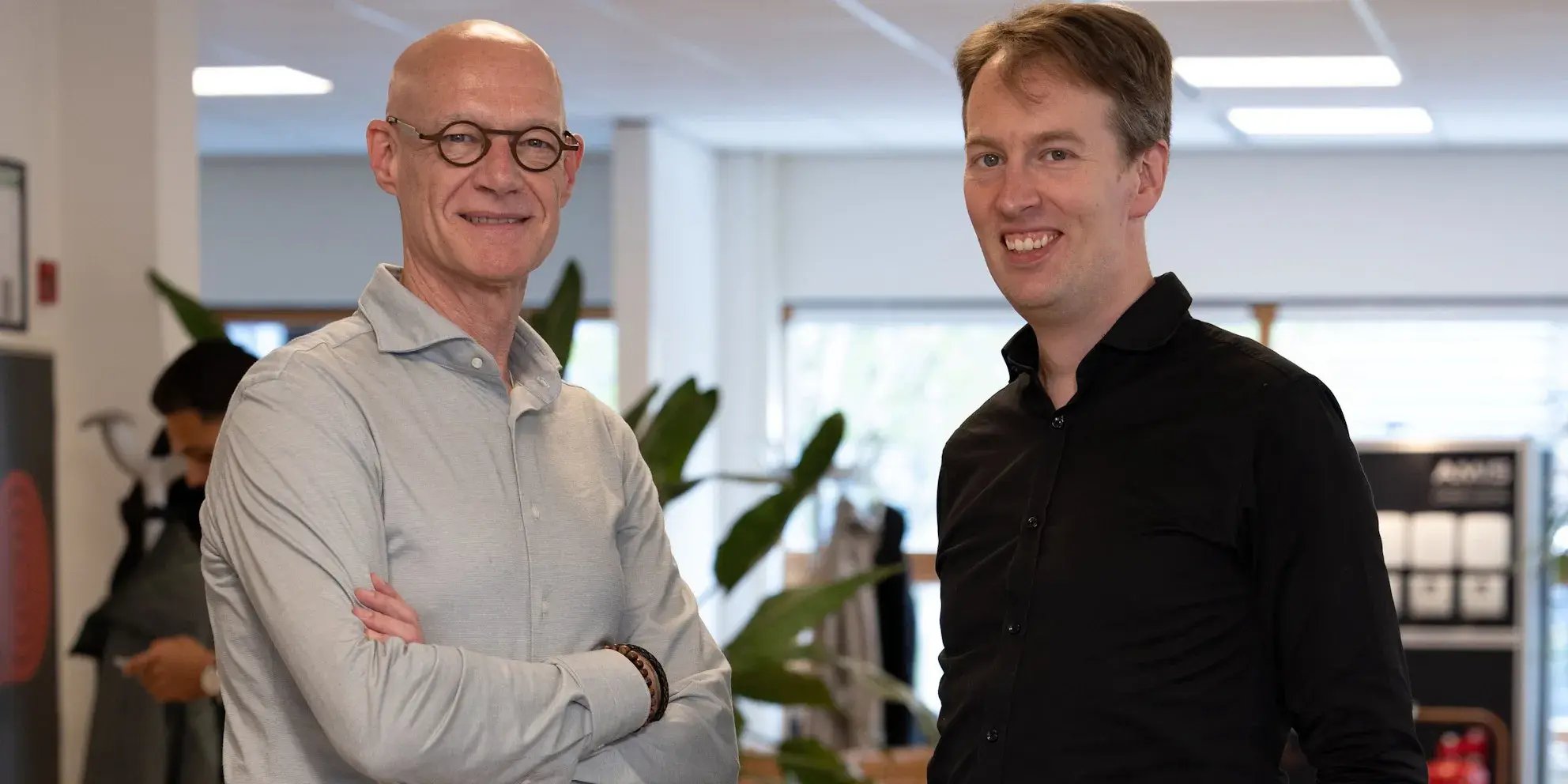 Twee mannen staan glimlachend naast elkaar in een kantooromgeving.