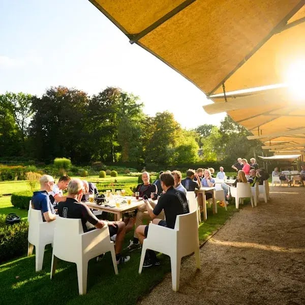 Een groep mensen zit buiten op een terras in de zon en geniet van eten en drinken.
