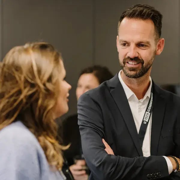A man in a dark blazer talks with a woman during a networking event.
