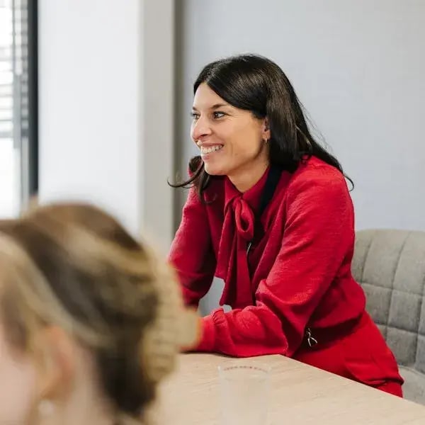 A woman in a red outfit smiles during a meeting or gathering.