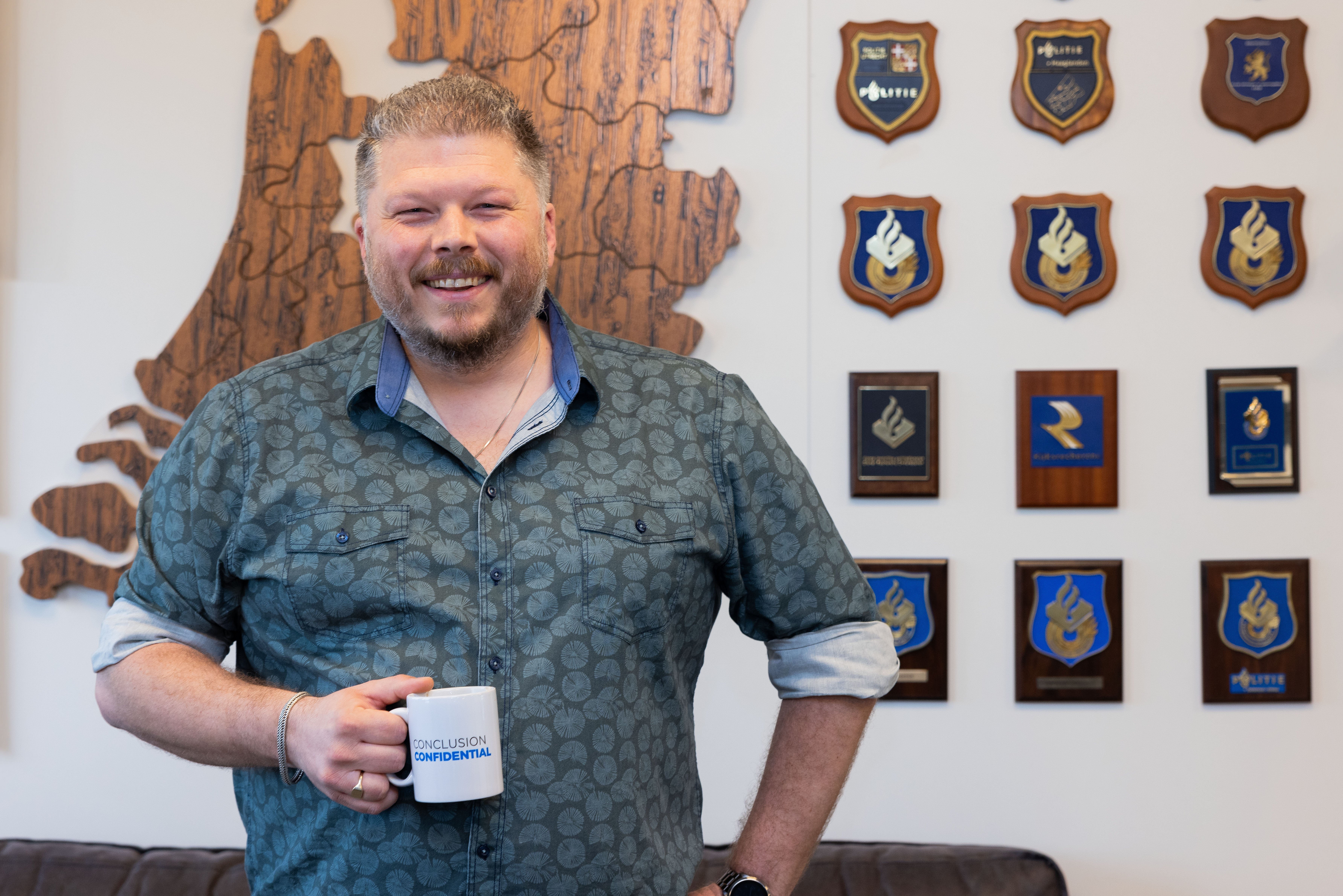 Man with a cup of coffee in an office with medals in the background.