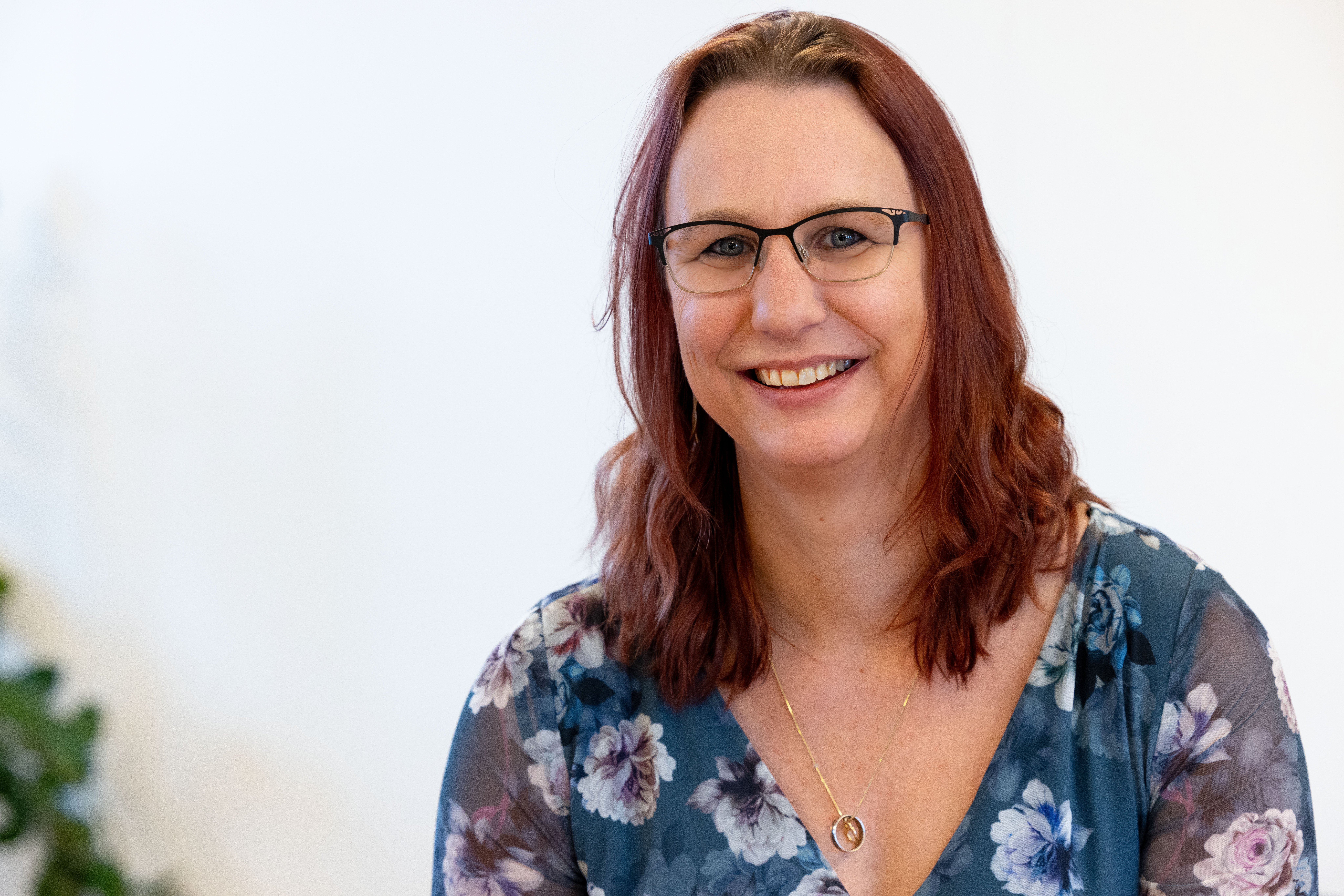 Woman wearing a floral blouse smiles at the camera in a bright office space.