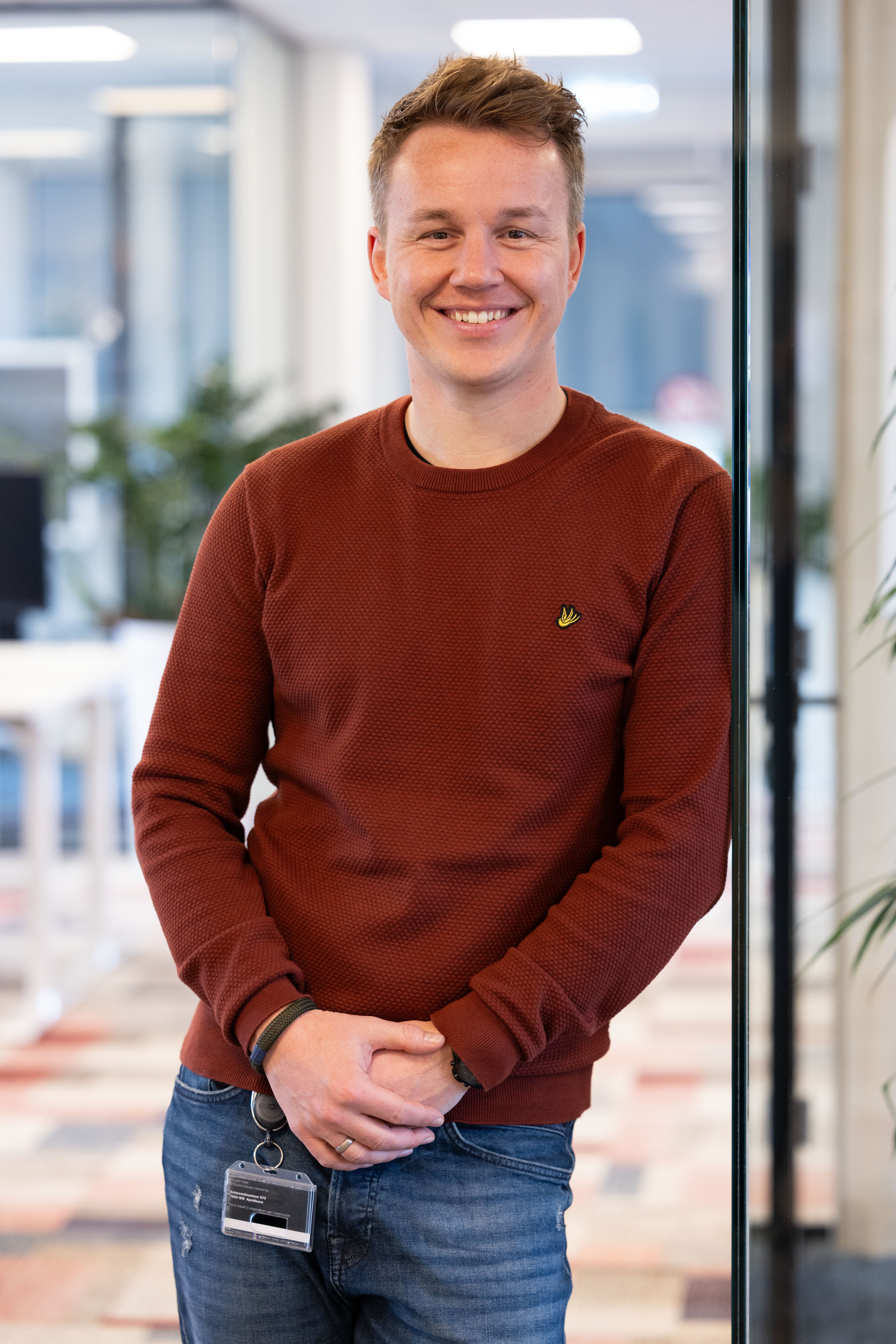 Man leunt tegen een deur aan en lacht voor zich uit.