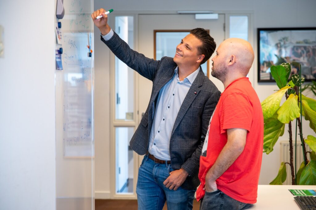 Two people discussing something on a whiteboard in an office.