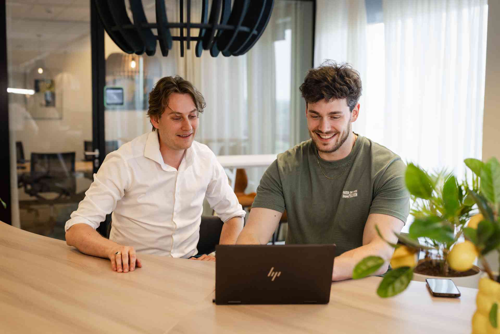 Two men look at a laptop in an office.
