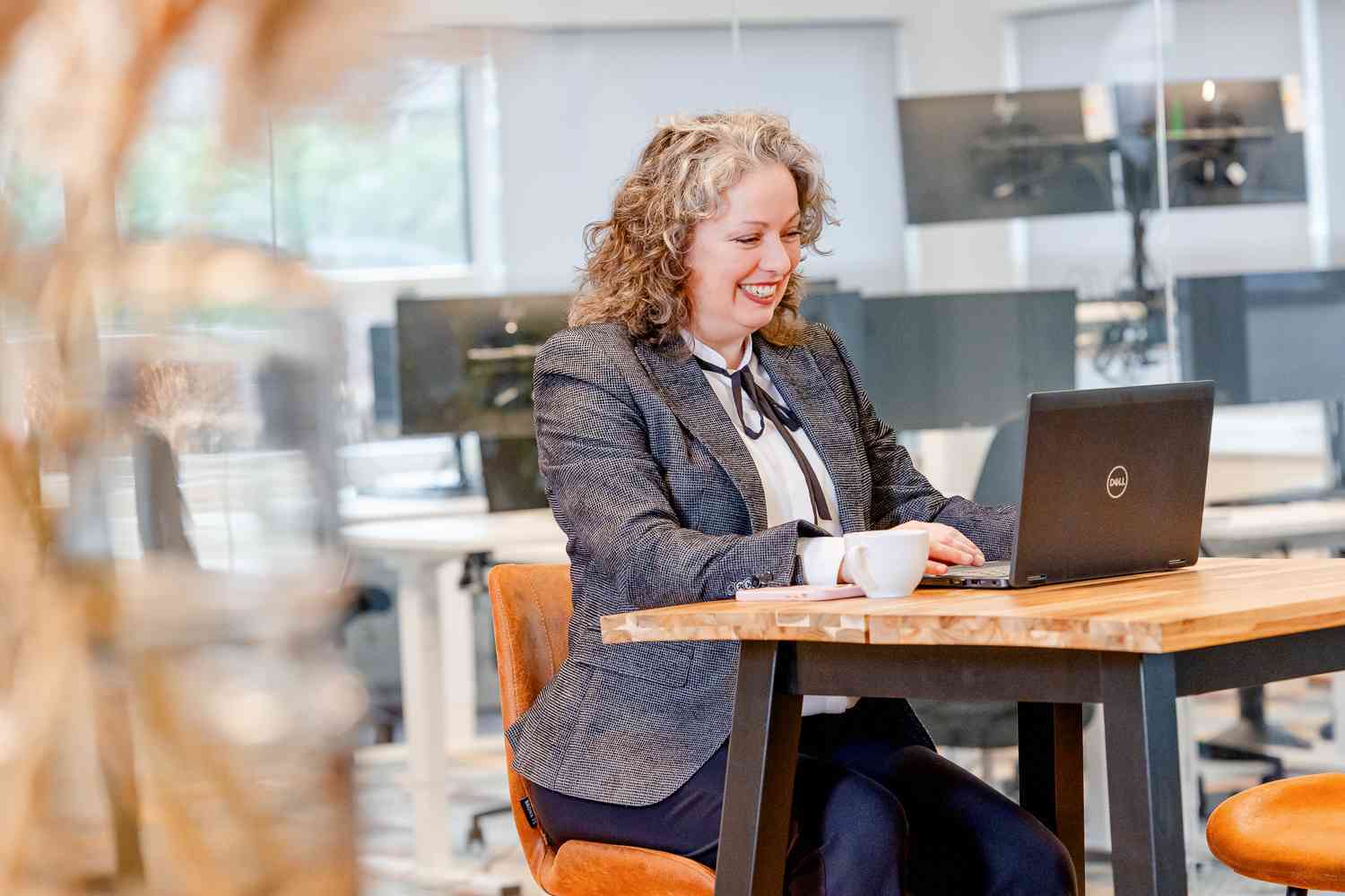 Vrouw werkt lachend achter een laptop aan een tafel.