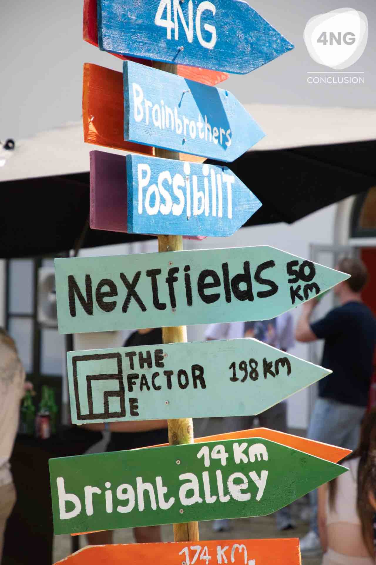 A colorful sign with arrows points the way to various destinations, such as '4NG' and 'Nextfields'.