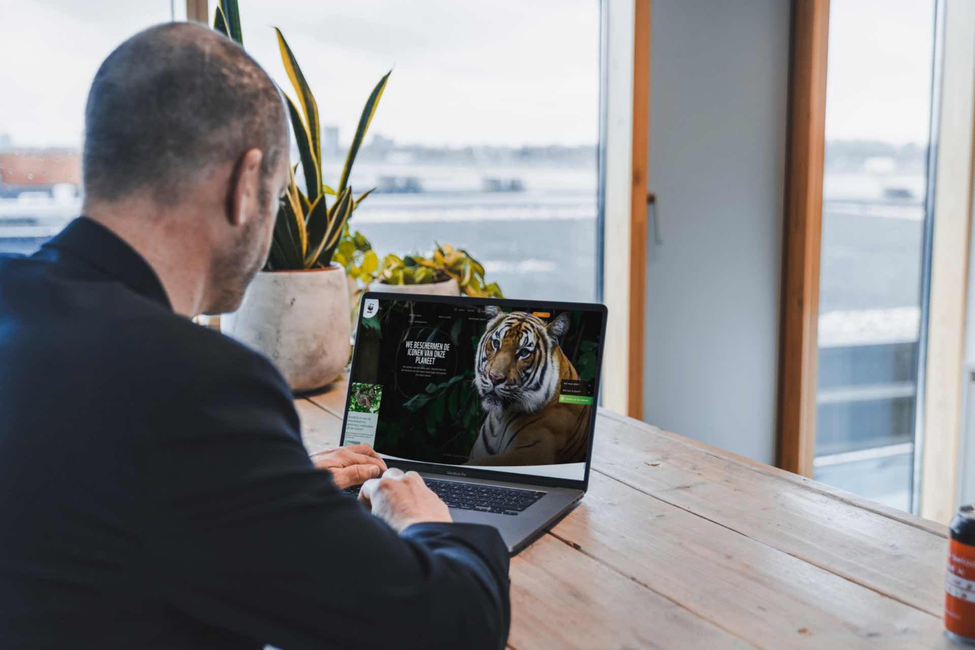 Een mannelijke collega zit aan een lange tafel en achter zijn laptop.