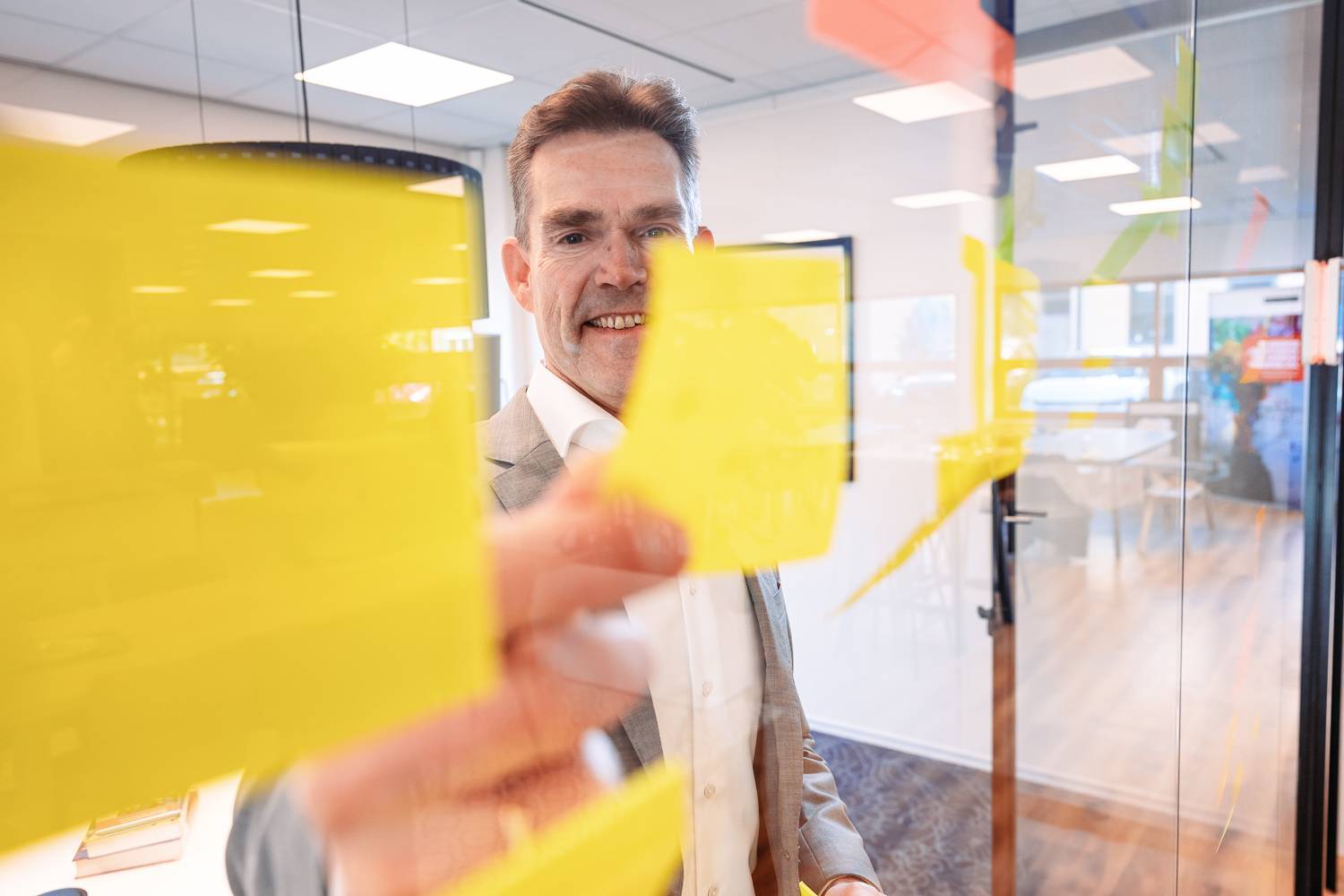 Man staat voor een raam met post-its en glimlacht terwijl hij ze vasthoudt.