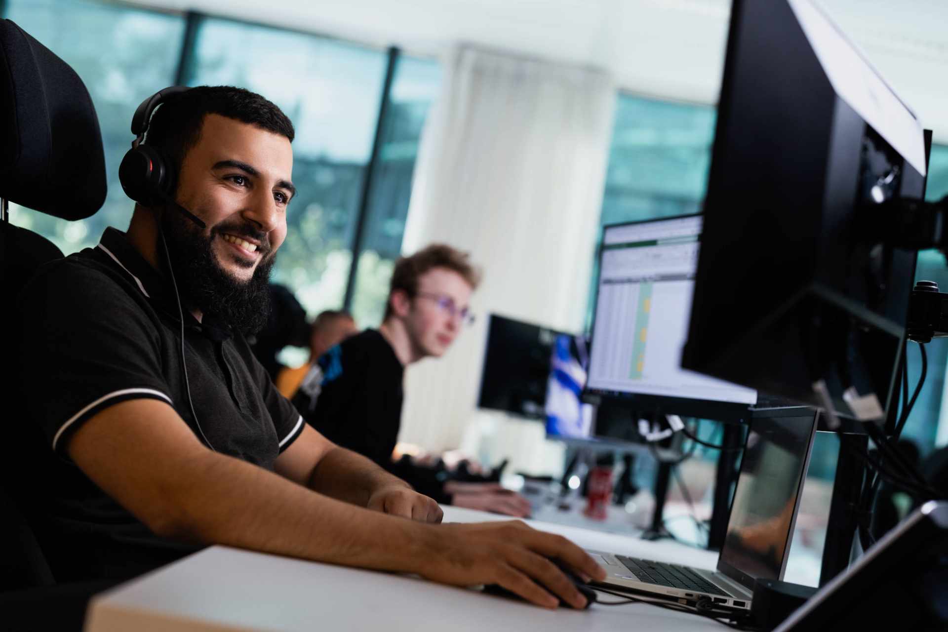 Man met koptelefoon op kijkt naar zijn scherm en beweegt de muis in zijn hand.