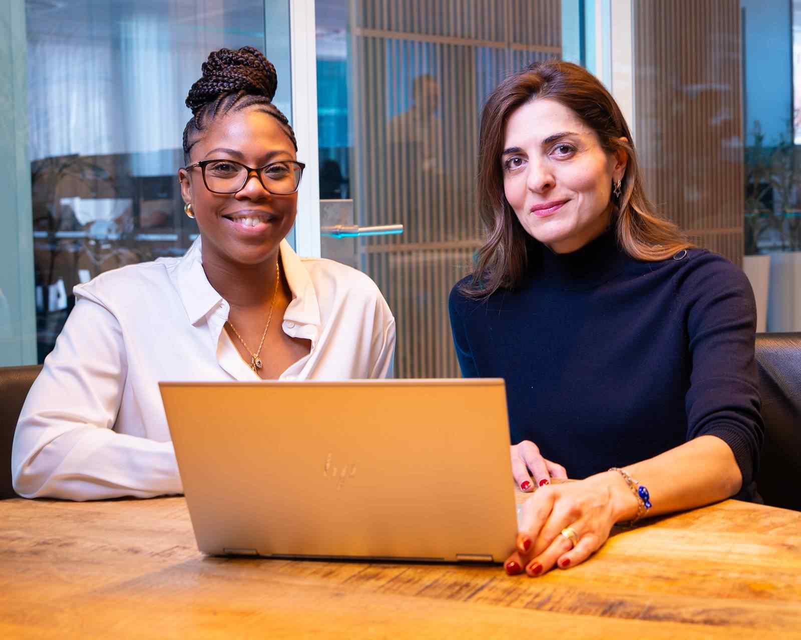 Two women work together on a laptop in a meeting room.