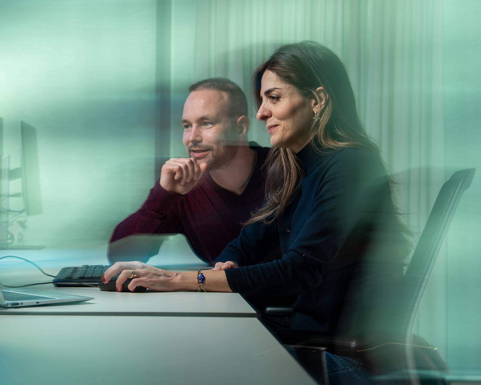 Two colleagues are working together on a computer, with their focus on the screen.