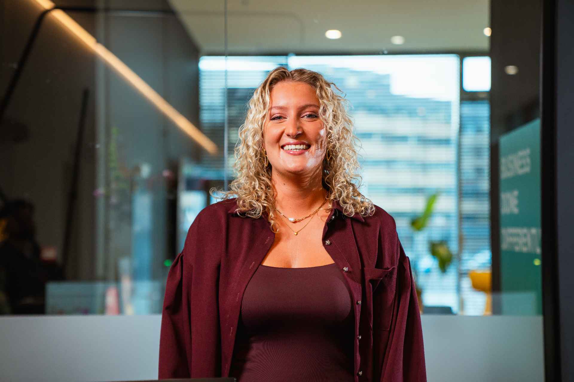 Vrouw met blond krullend haar in het bordeaux gekleed lacht in de camera