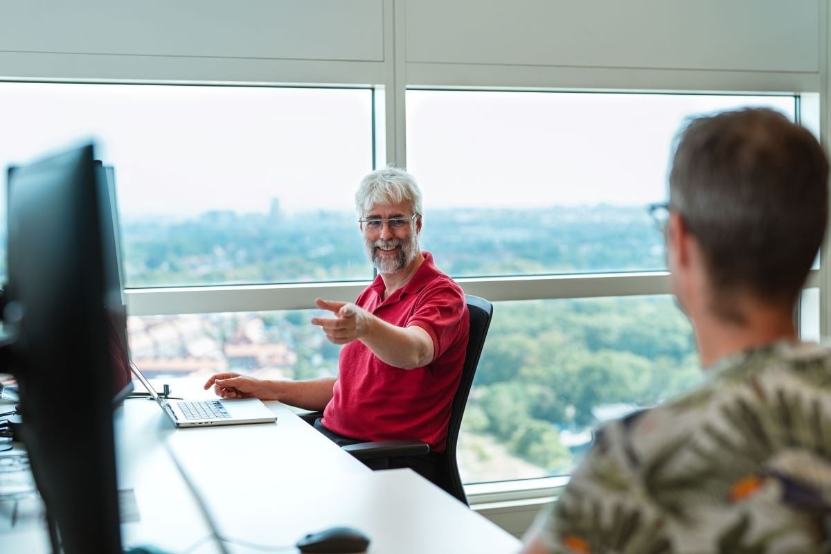Een collega legt iets met zijn handen uit aan de collega die naast hem zit.