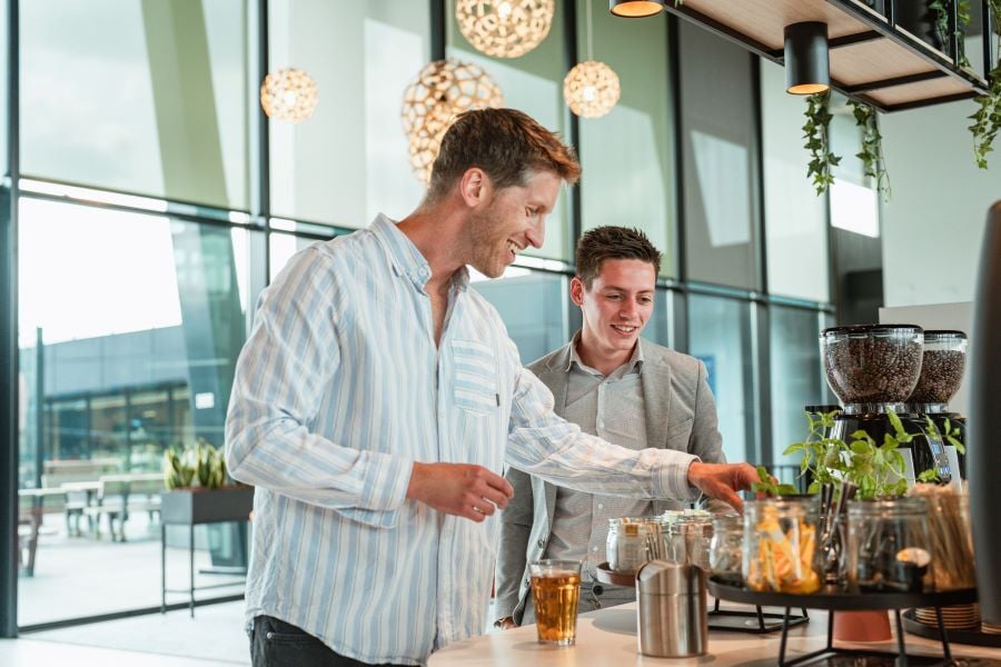 Two men in a modern workspace, laughing at the coffee bar.