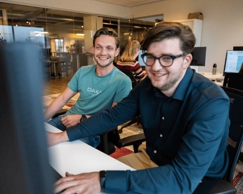 Twee mannen kijken enthousiast naar hun computerscherm.