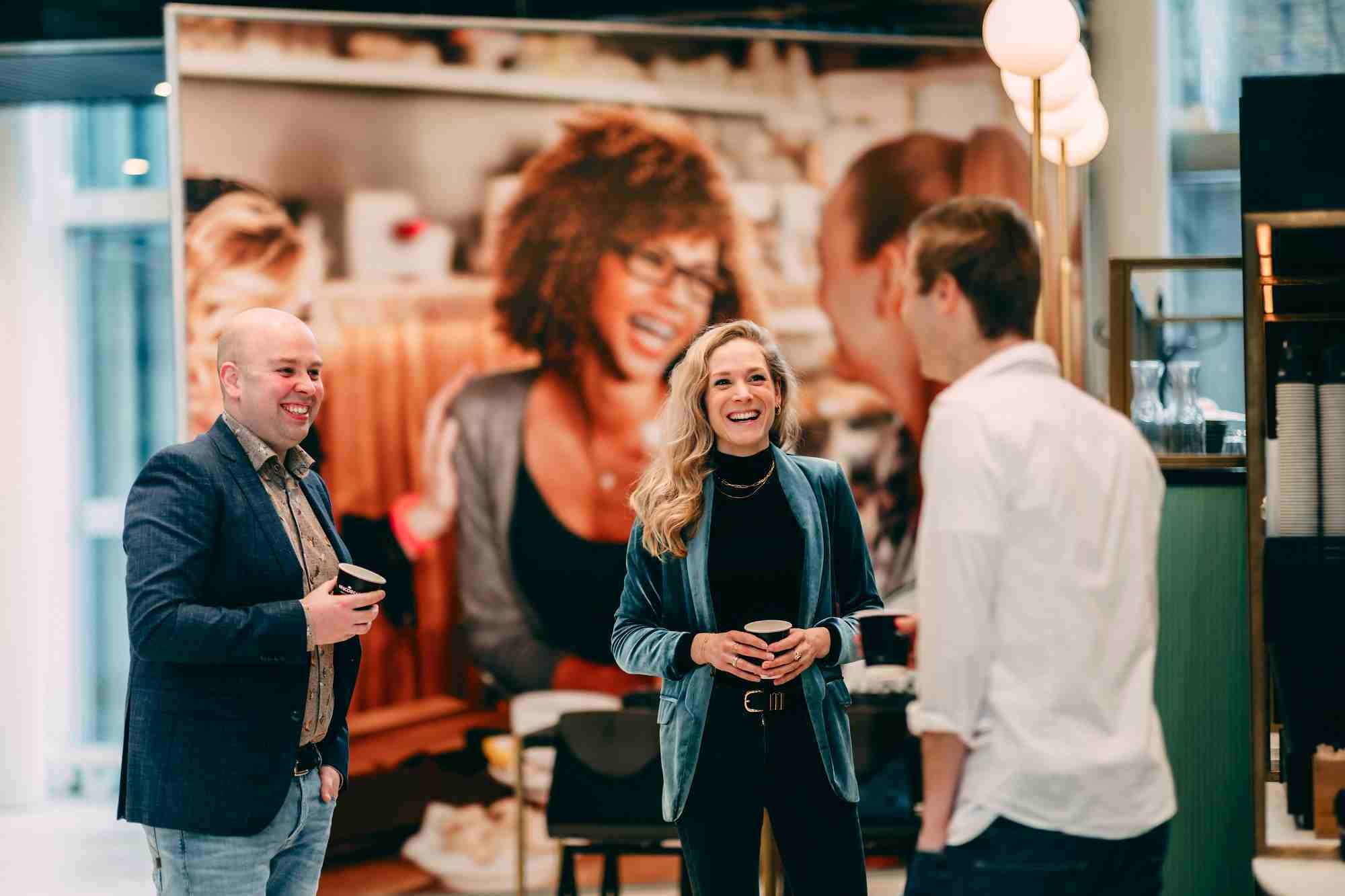 Three people laughing and talking with coffee in hand.
