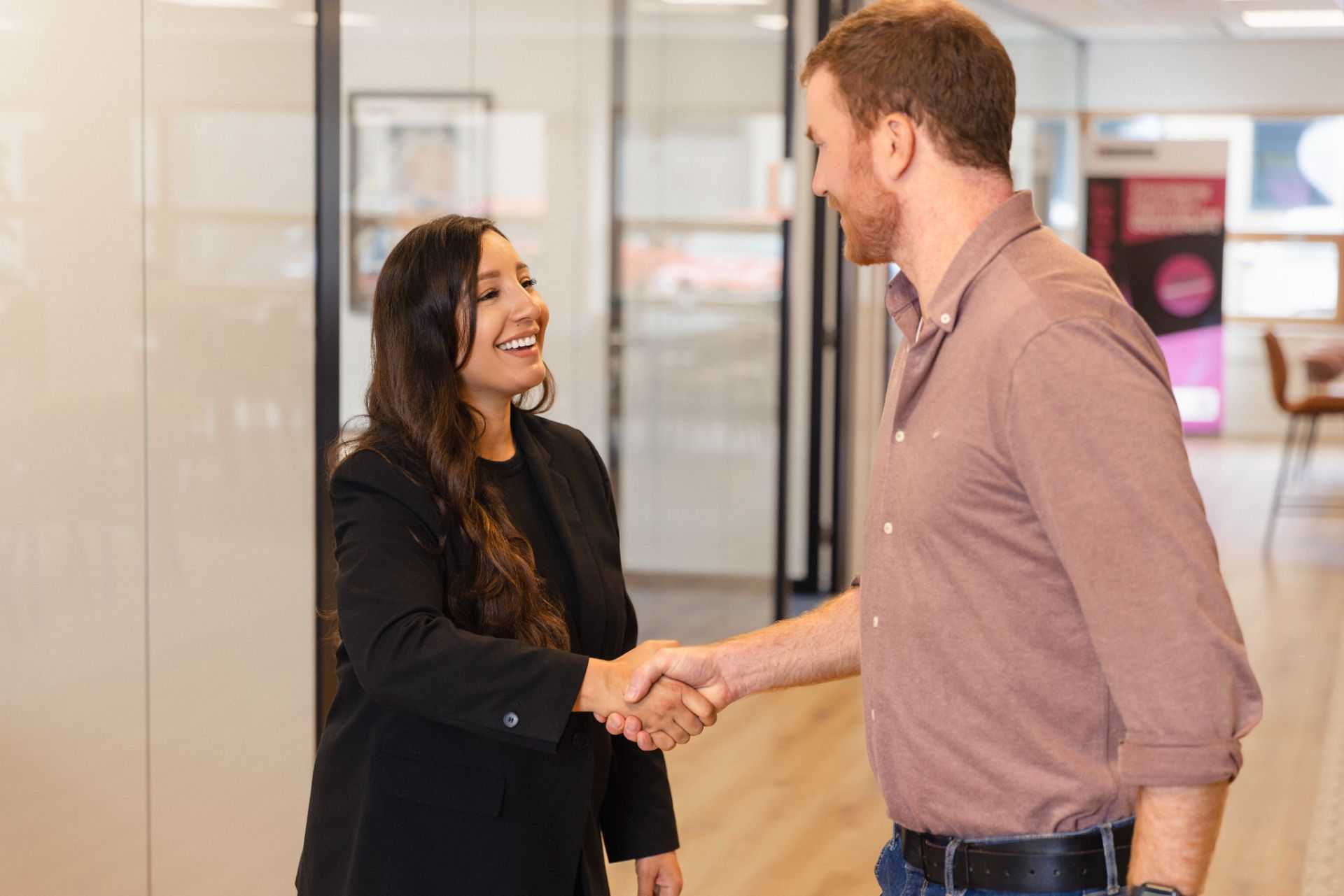 Two people shake hands and smile in an office.