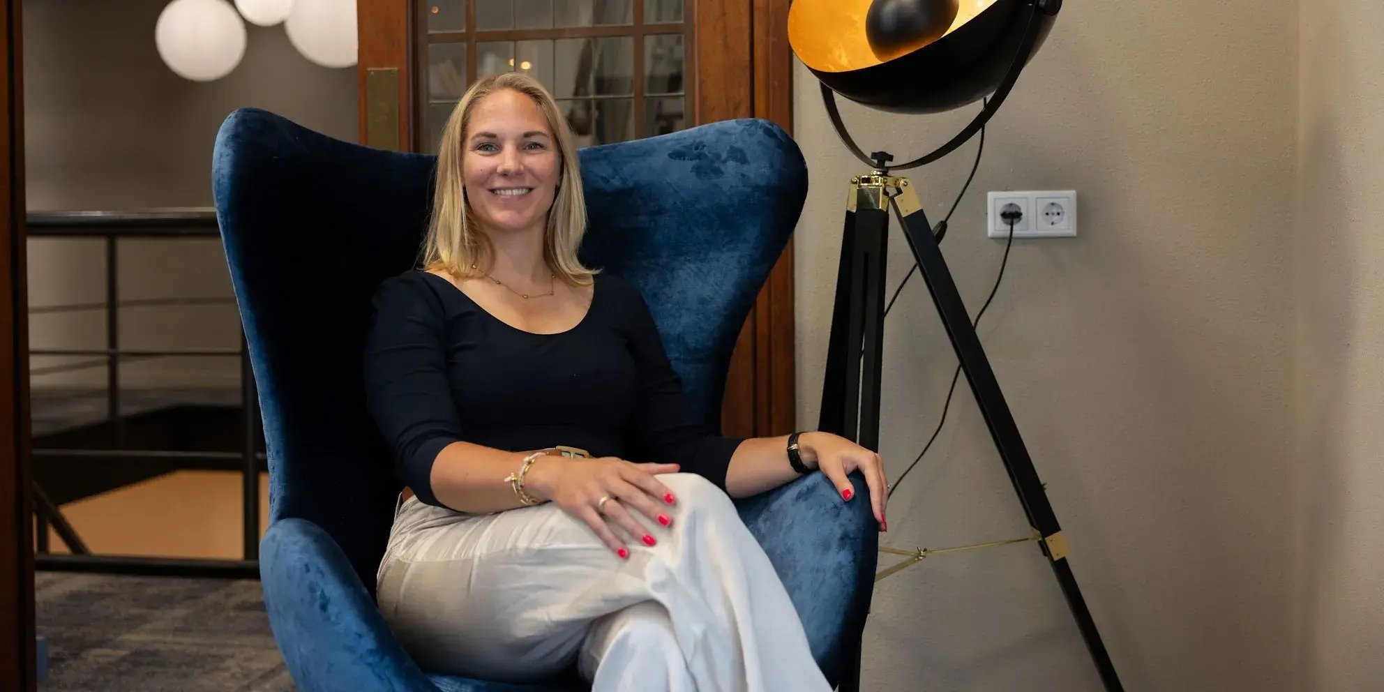 Vrouw glimlacht terwijl ze ontspannen in een blauwe stoel zit.