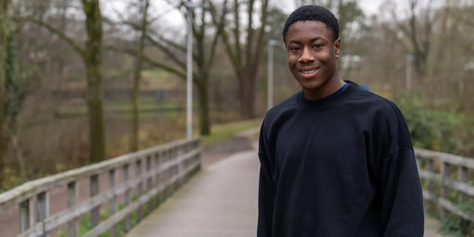 Man glimlacht buiten op een brug in een bosrijke omgeving.