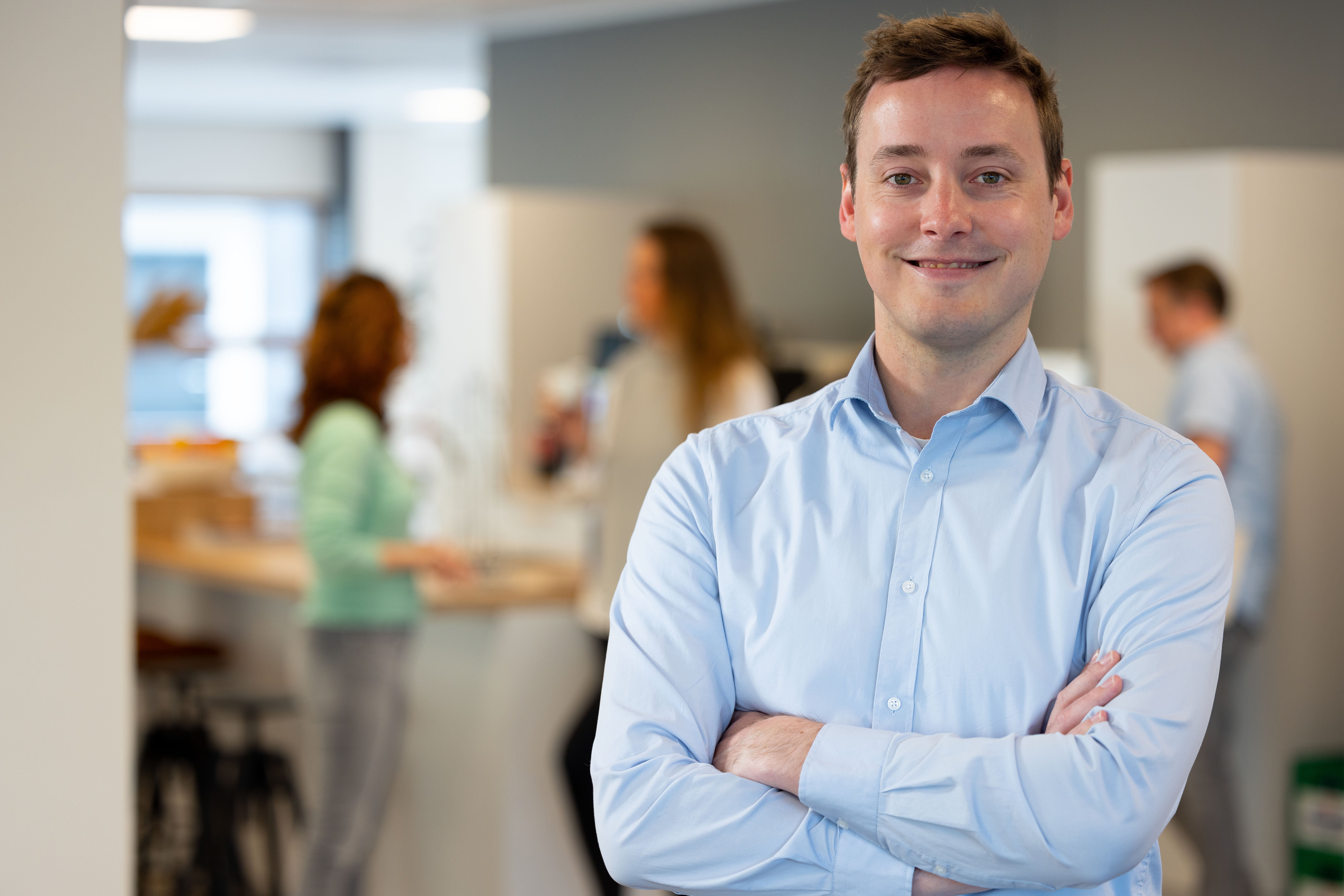 Mannelijke collega in blauwe blouse met armen gekruist lachend naar de camera