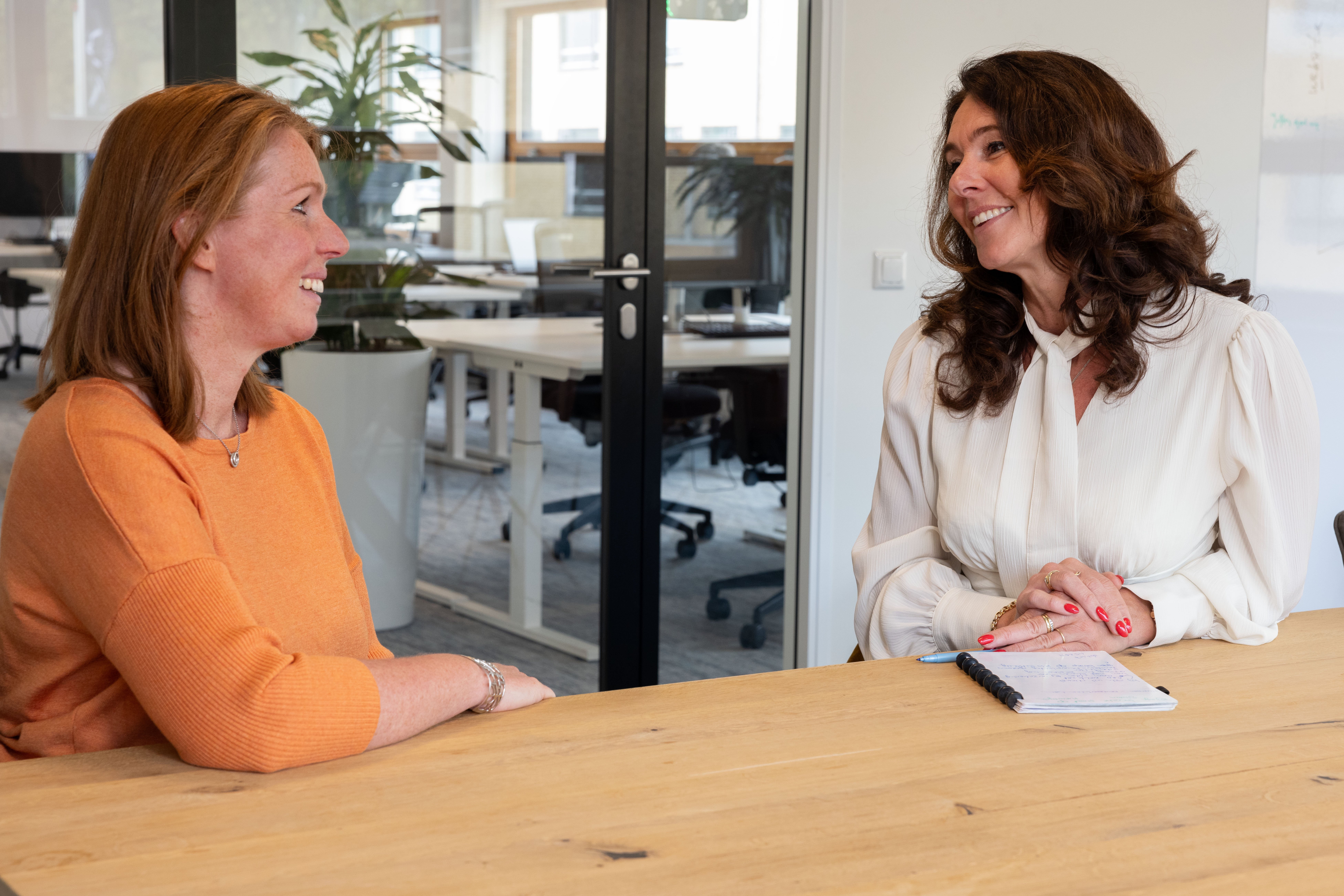 Twee vrouwen die aan een bureau zitten te lachen naar elkaar