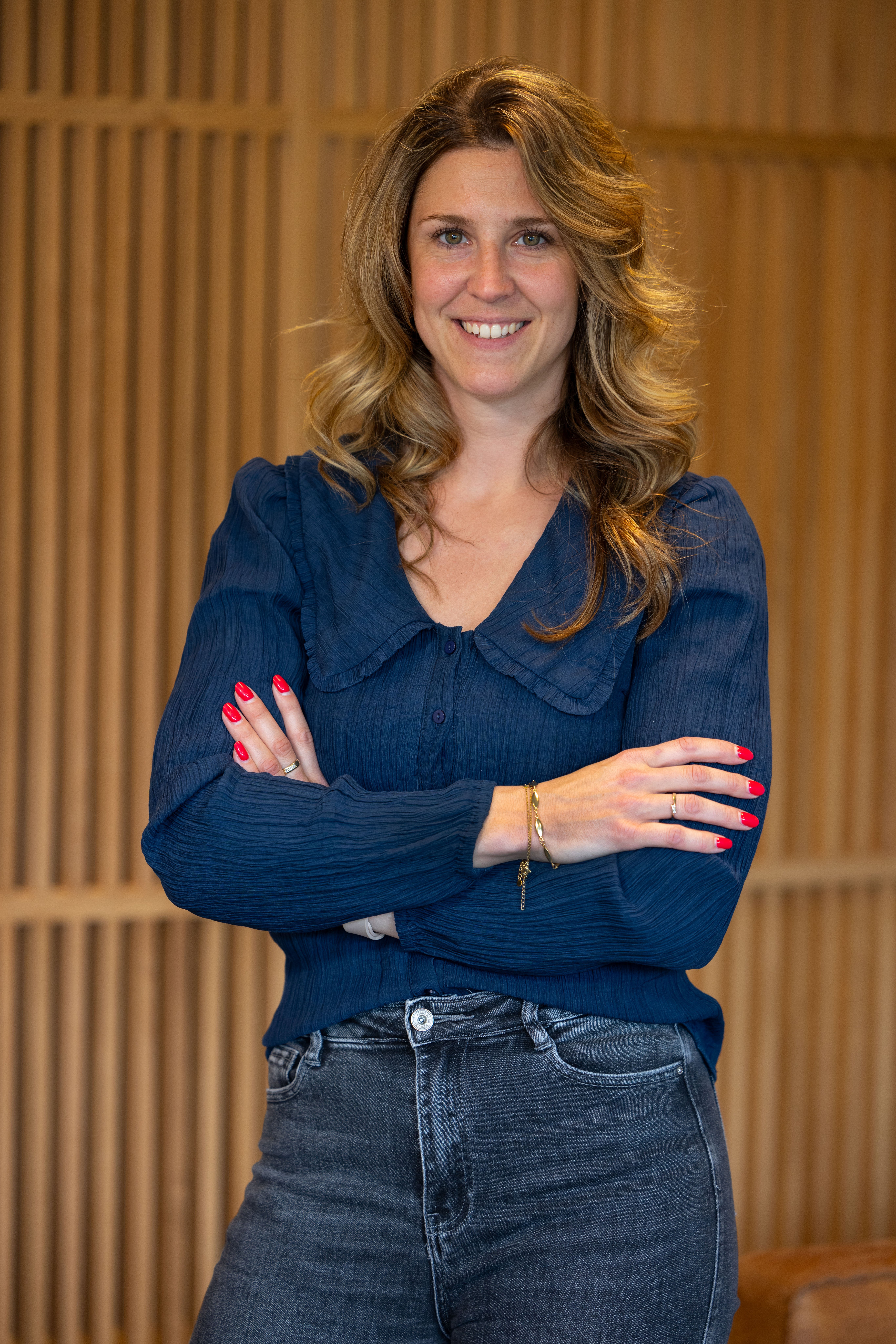 Vrouwe collega in donker blauwe blouse met armen over elkaar lachend naar de camera