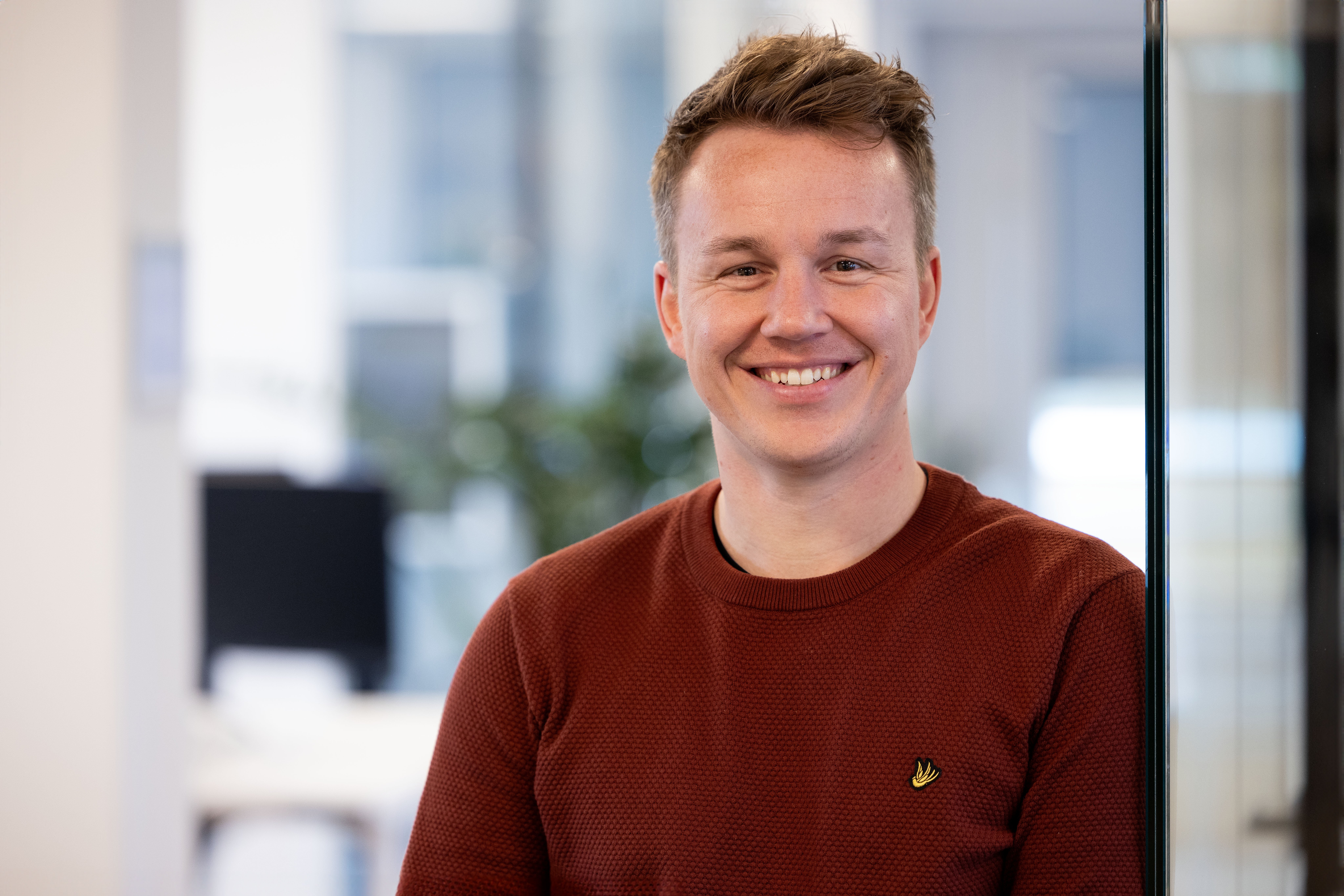 Mannelijke collega in donker rode trui lachend naar de camera