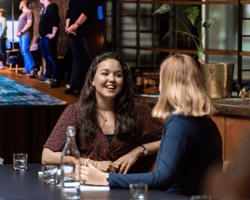 Twee vrouwen zitten met elkaar aan tafel en kletsen.