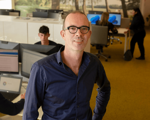 Staff member in an open office environment with laptops and desks.