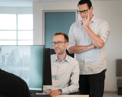 Two colleagues laughing at a desk in a modern office.