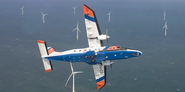 Vliegtuig in de lucht over de zee waar windmolens in staan