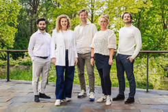 Group of five people pose outside in front of a green background.