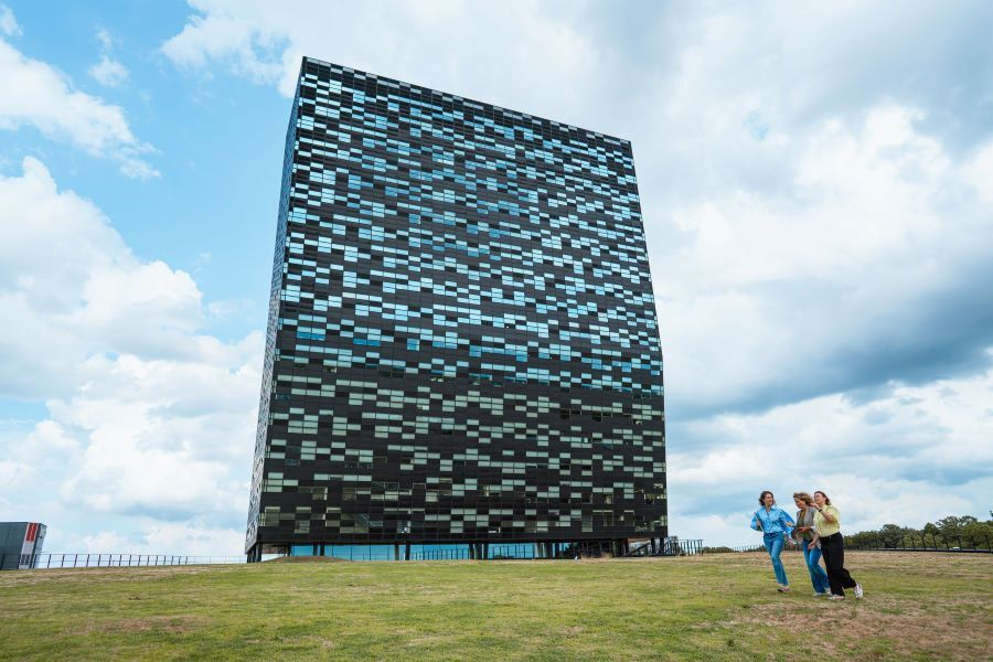 A modern company building with three employees walking outside, with a green lawn and a clear sky in the background.