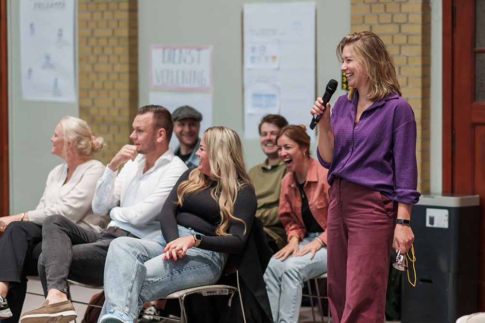 A woman speaks into a microphone while a group of people listen.