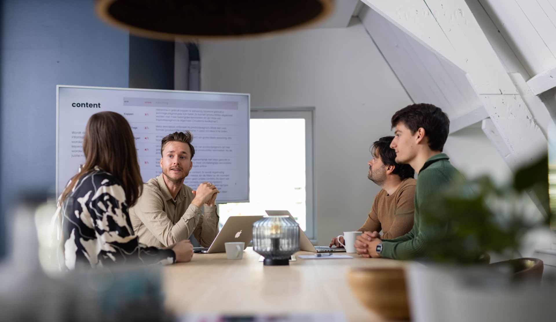 A man presents to three colleagues in a meeting room.
